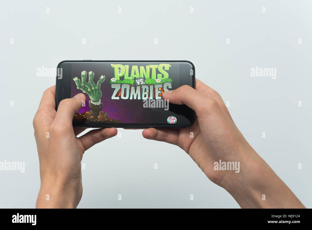 Samara, Russland-07, 29, 2019: ein junger Kerl spielt eine Pflanzen gegen Zombies Spiel auf dem Iphone 8 Plus. Teenager hält ein Handy in der Hand mit einem Spiel Pflanzen gegen Zombies mobile auf einem weißen Hintergrund. Stockfoto