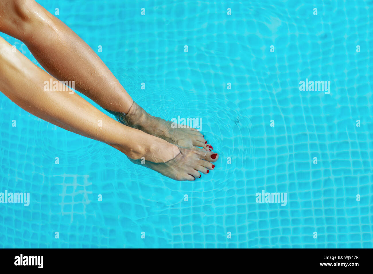 Schöne gebräunte weibliche Beine im Wasser im Pool. Stockfoto