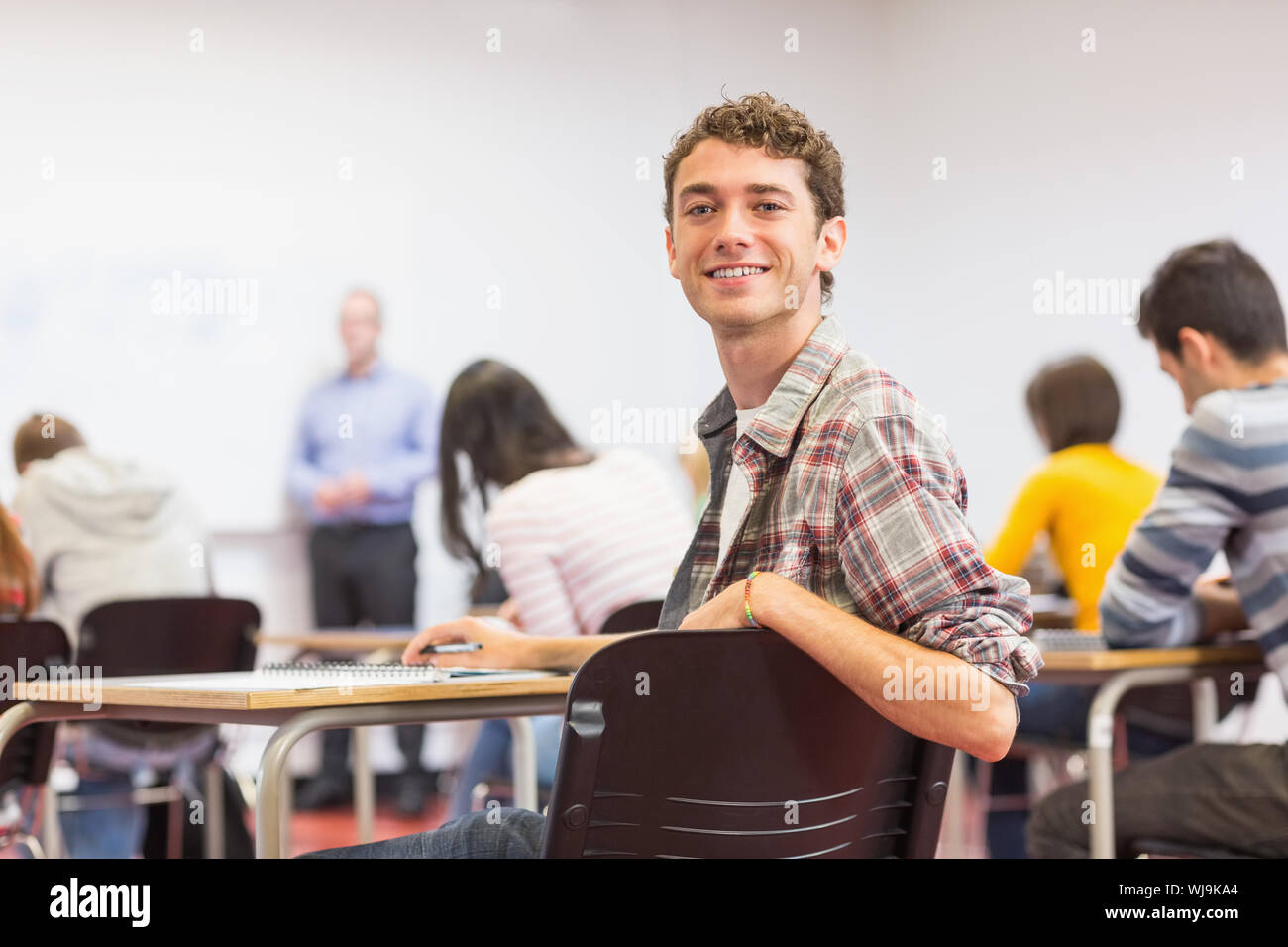 Porträt eines lächelnden jungen männlichen Schüler mit Lehrern und anderen im Klassenzimmer verschwommen Stockfoto