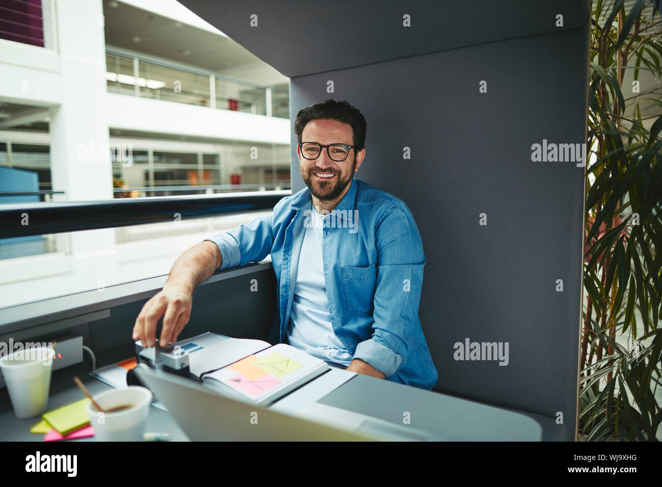 Lächelnd Creative Professional über Noten und arbeitet an einem Laptop, während allein in einem Büro pod Stockfoto