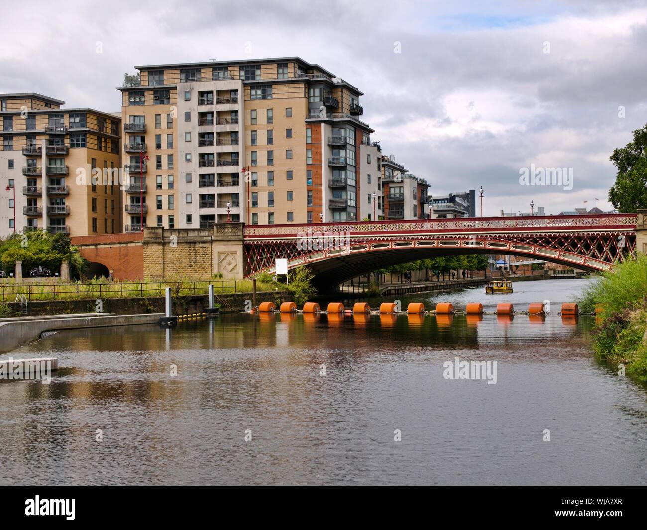 Rote Brücke über den Fluss Aire mit orange Ausleger mit Yellow River Taxi im Hintergrund und Wohnungen in Leeds Yorkshire England Stockfoto