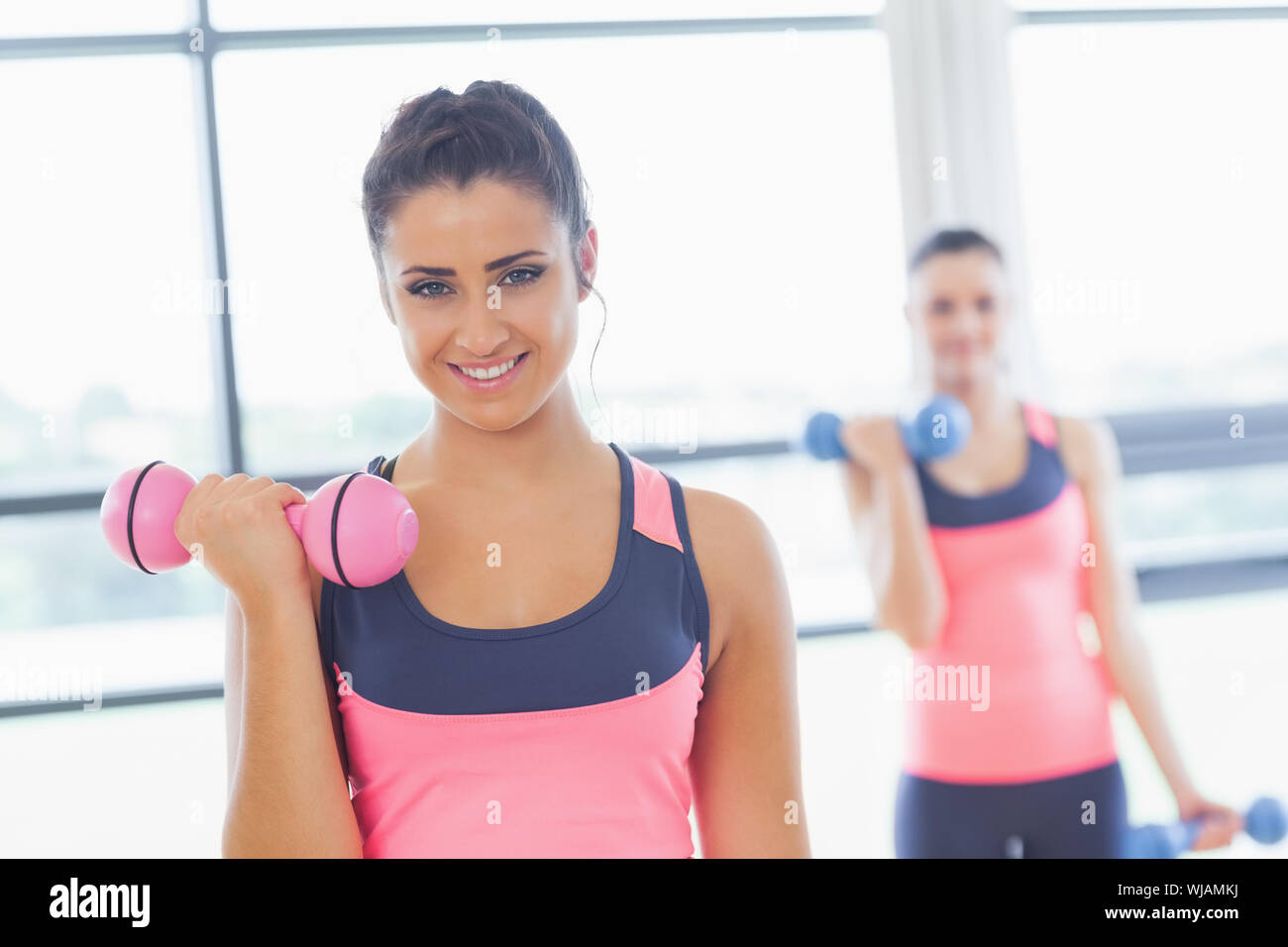 Fit Woman Hantel Krafttraining mit Freund im Hintergrund in Turnhalle Stockfoto