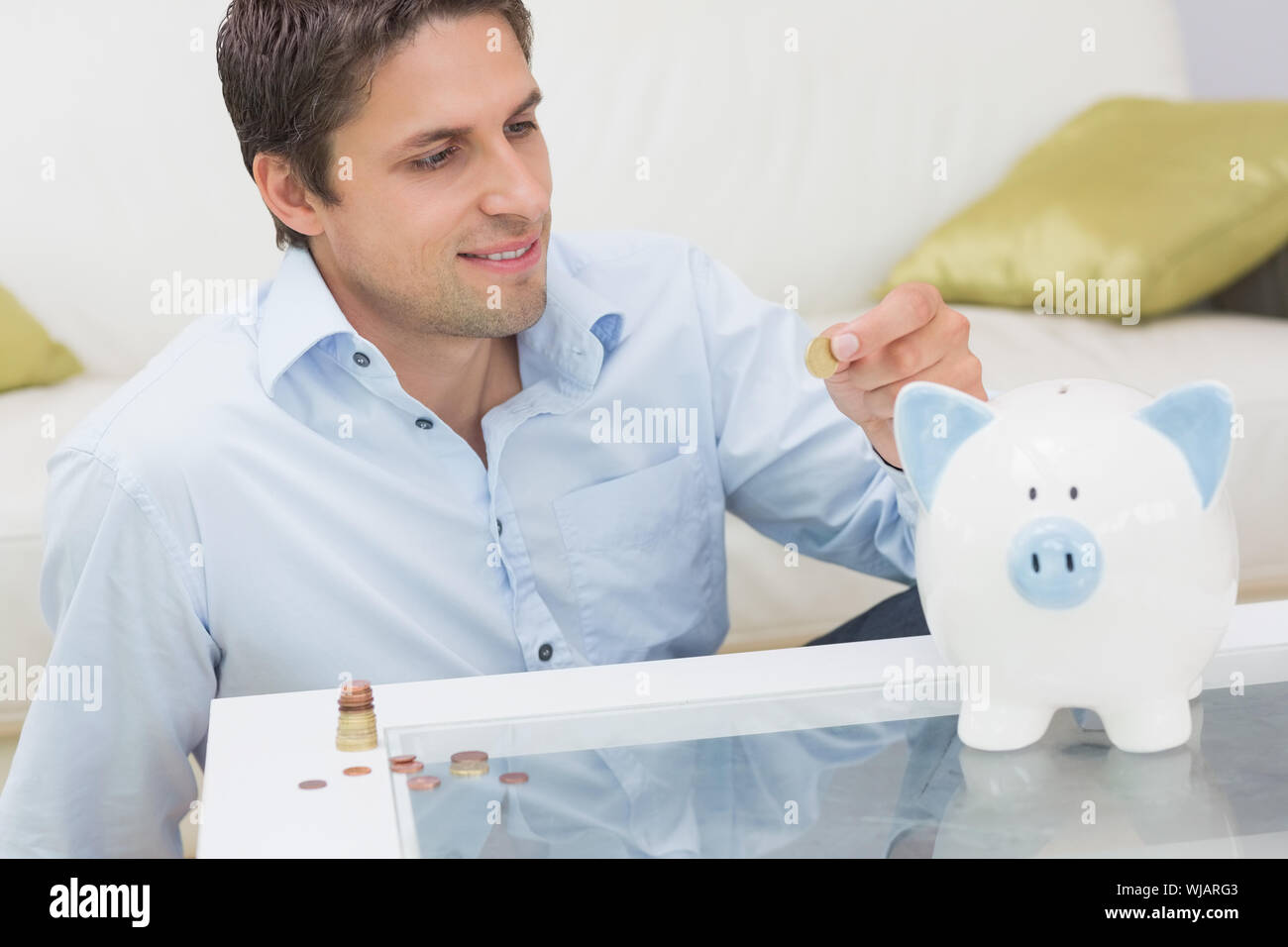 Legerer Mann setzen einige Münzen in ein Sparschwein im Wohnzimmer Stockfoto