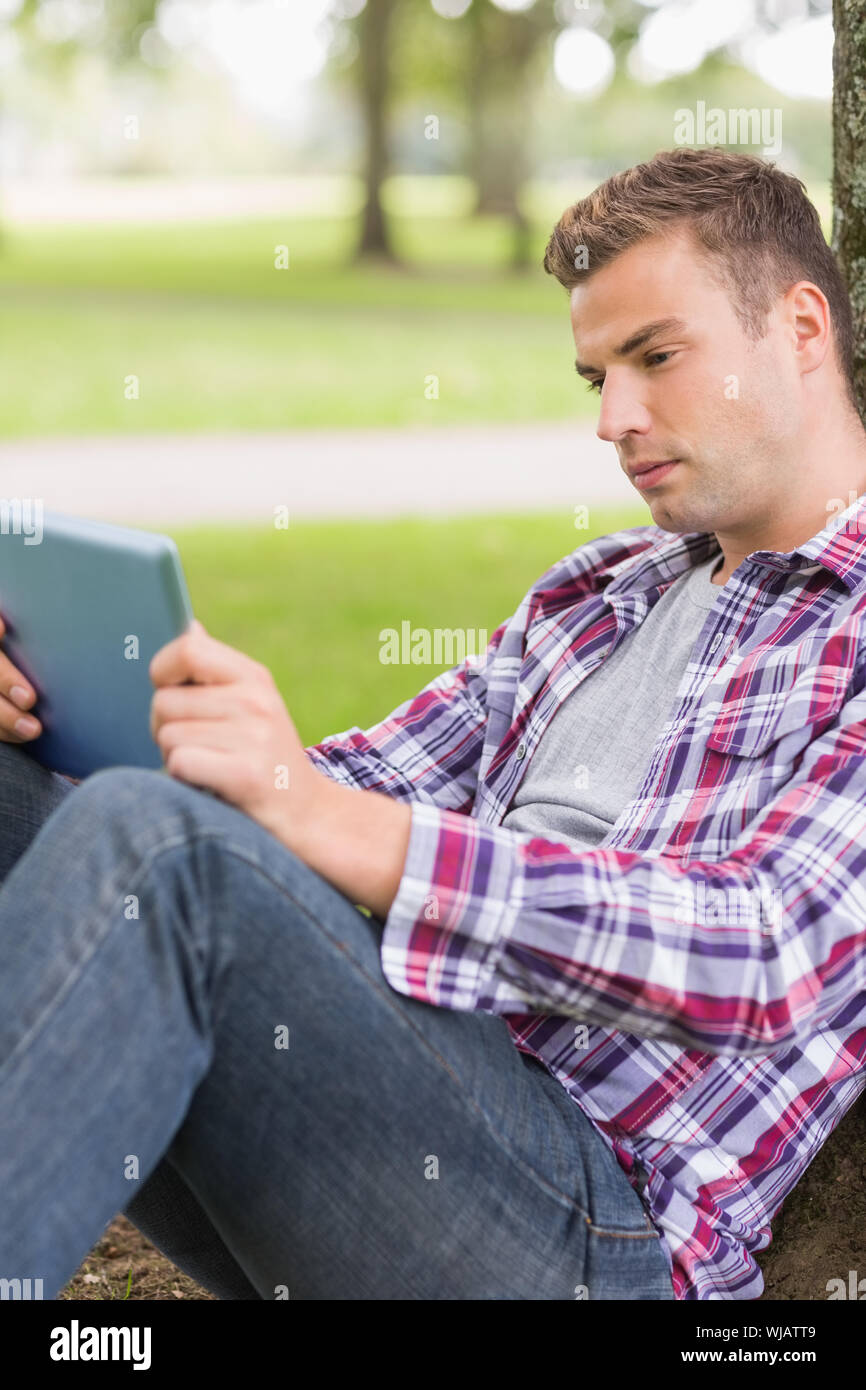 Ernsthaften Studenten mit seinem Tablet-pc außerhalb stützte sich auf Baum Stockfoto