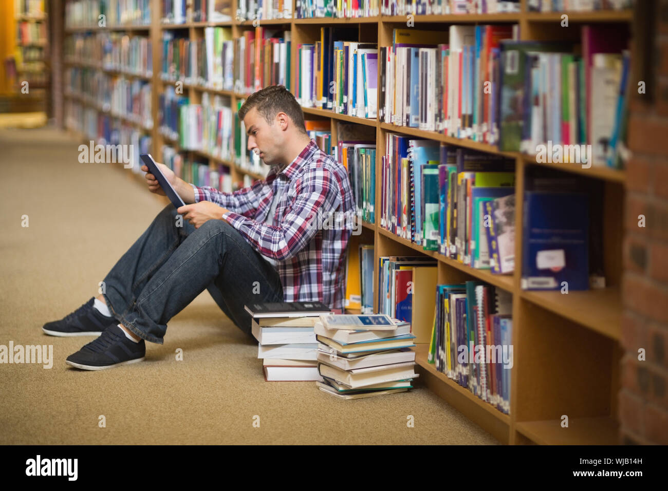 Konzentrierte sich jungen Studenten sitzen auf Bibliothek Boden mit tablet Stockfoto