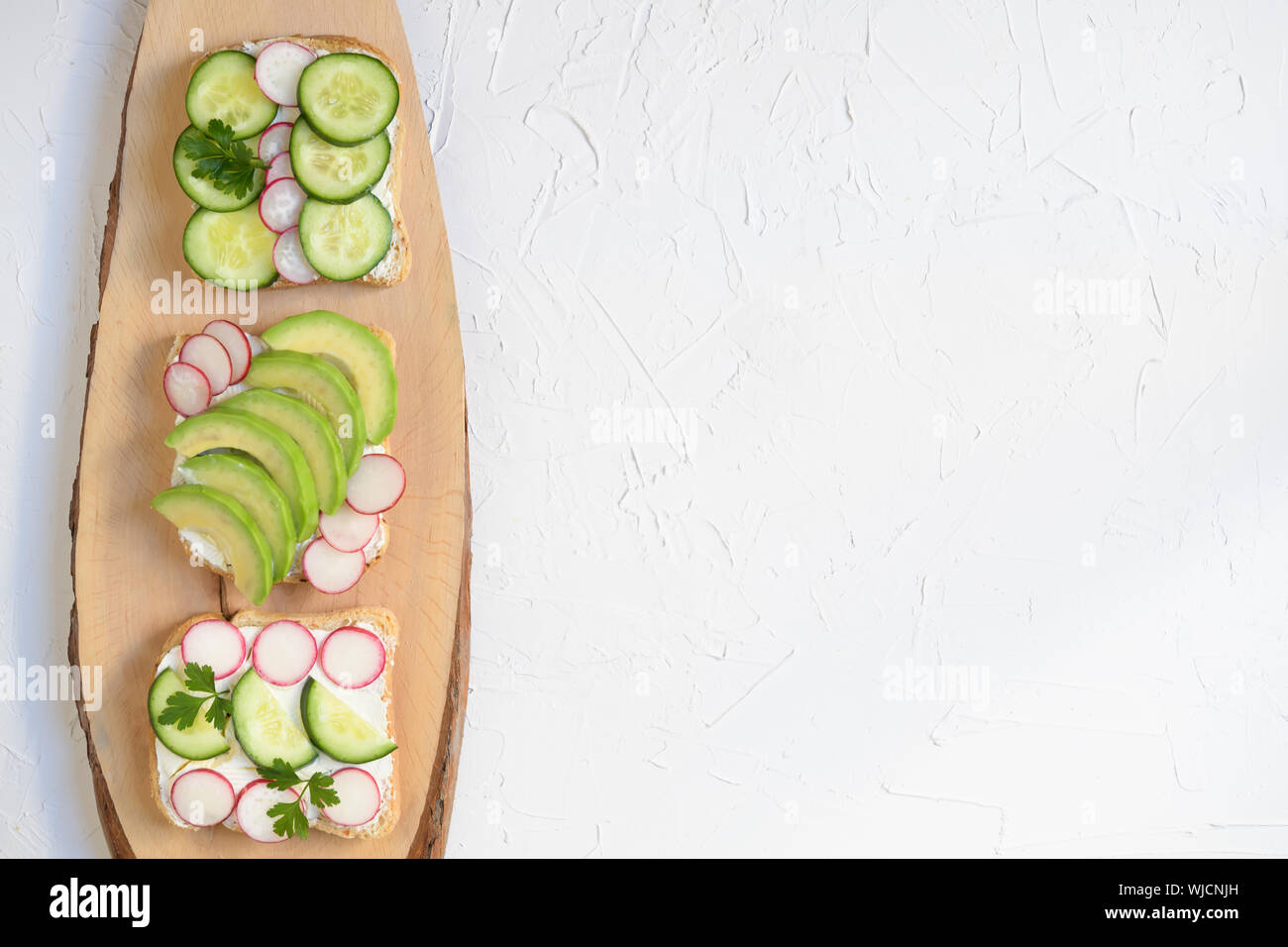 Drei vegetarische o vegan Sandwich mit Avocado, Rettich, Gurke und frischer Käse, gesunden Snack für Kinder und Erwachsene, einfach zuzubereiten, Ansicht von oben, h Stockfoto