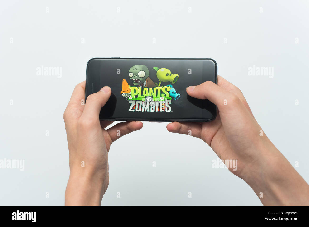 Samara, Russland-07, 29, 2019: ein junger Kerl spielt eine Pflanzen gegen Zombies Spiel auf dem Iphone 8 Plus. Teenager hält ein Handy in der Hand mit einem Spiel Pflanzen gegen Zombies mobile auf einem weißen Hintergrund. Stockfoto