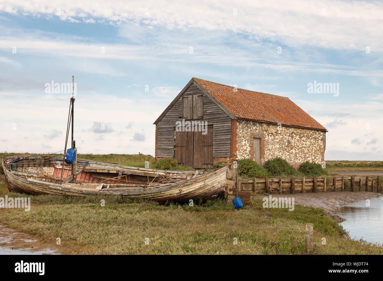 Ein Bild von einem alten Kohle Scheune und Fischerboot auf einer Wasserstraße bei Thornham, Norfolk, England, UK. Stockfoto