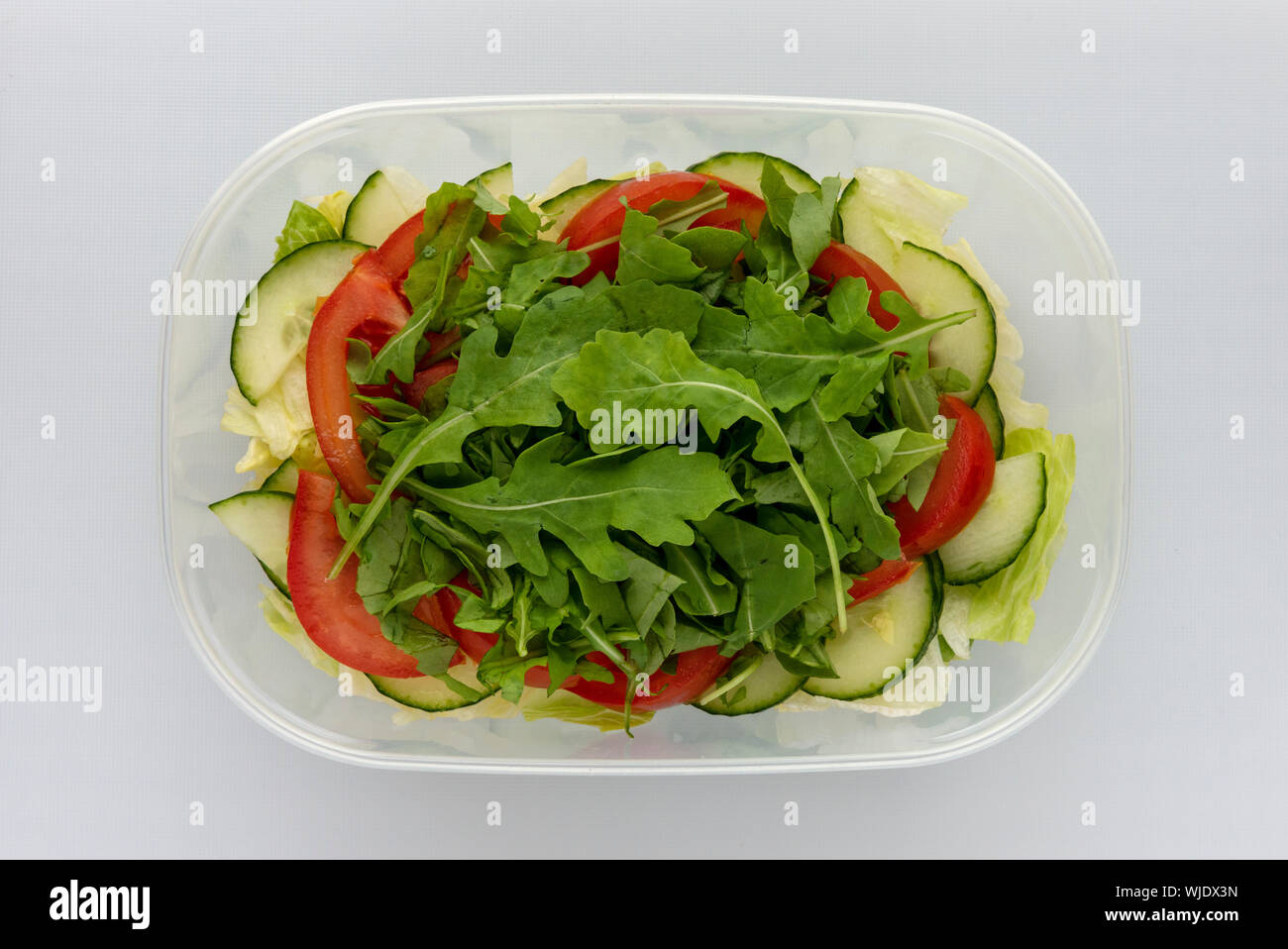 Blick von oben auf die hausgemachte geschichteten Salat in Plastik Schüssel auf weiße Oberfläche. Tomaten Gurken Rakete Blätter Eisbergsalat von oben. Stockfoto