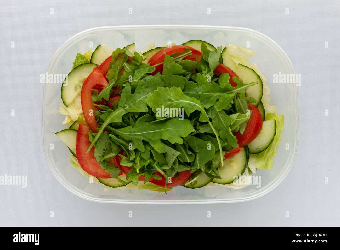 Hausgemachter, mehrschichtiger Salat in einer Plastikschale mit Tomaten-Gurkenkrake, Eisbergsalat von oben Stockfoto
