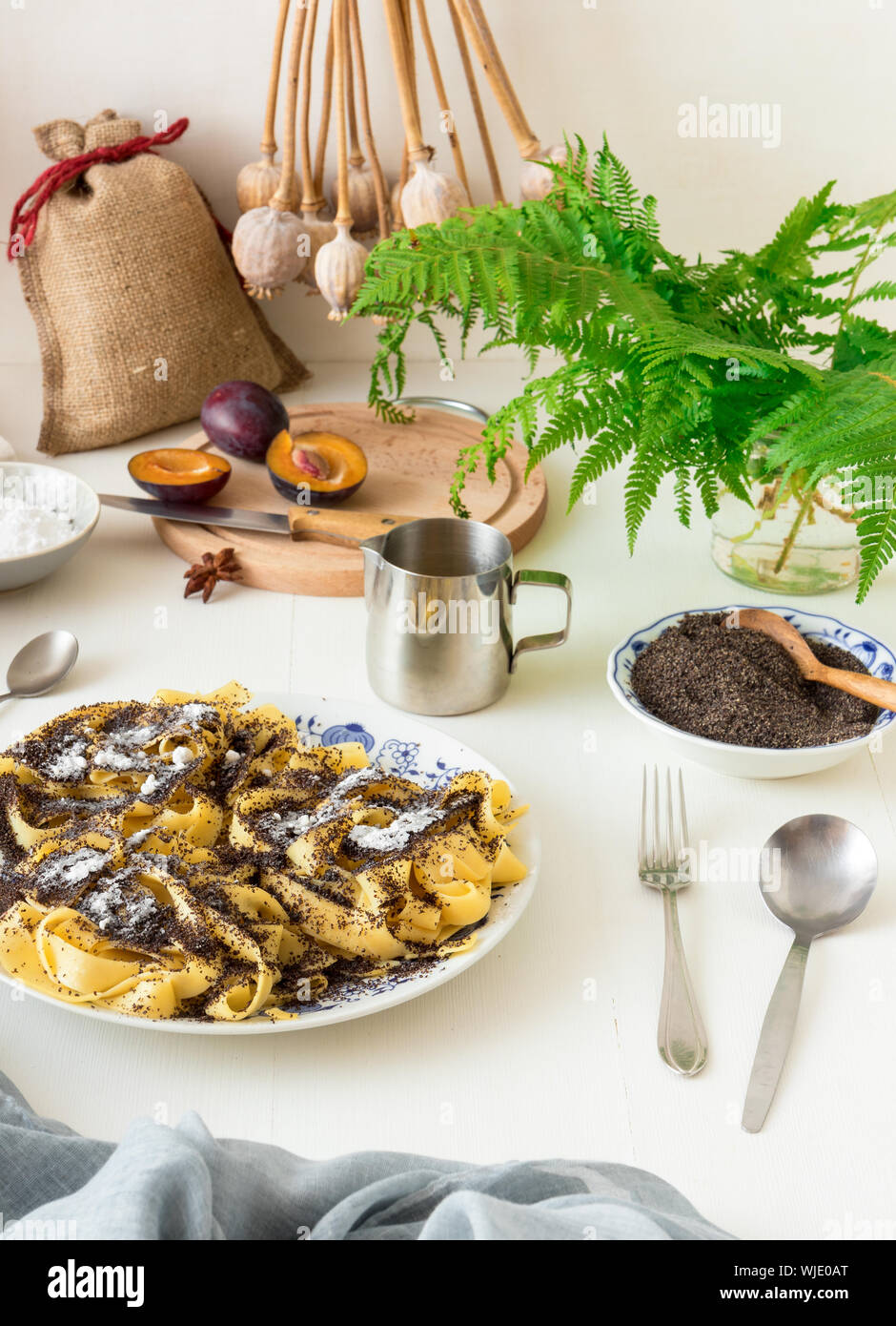 Süße Nudeln Dessert, Nudeln mit Mohn, Pflaumenkompott aus frischen Pflaumen, dunklen Hintergrund, weiße Holztisch mit frischen Blumen dekoriert. Trockene wh Stockfoto