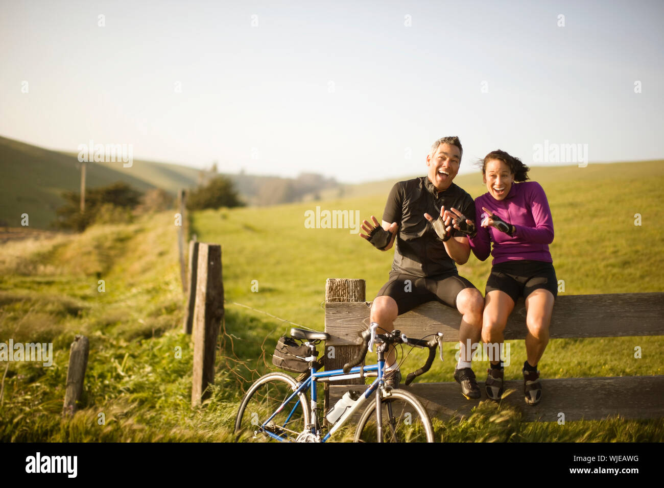 Männliche und weibliche Radfahrer sitzen auf einem Zaun ihre Hände winken und Lachen Stockfoto