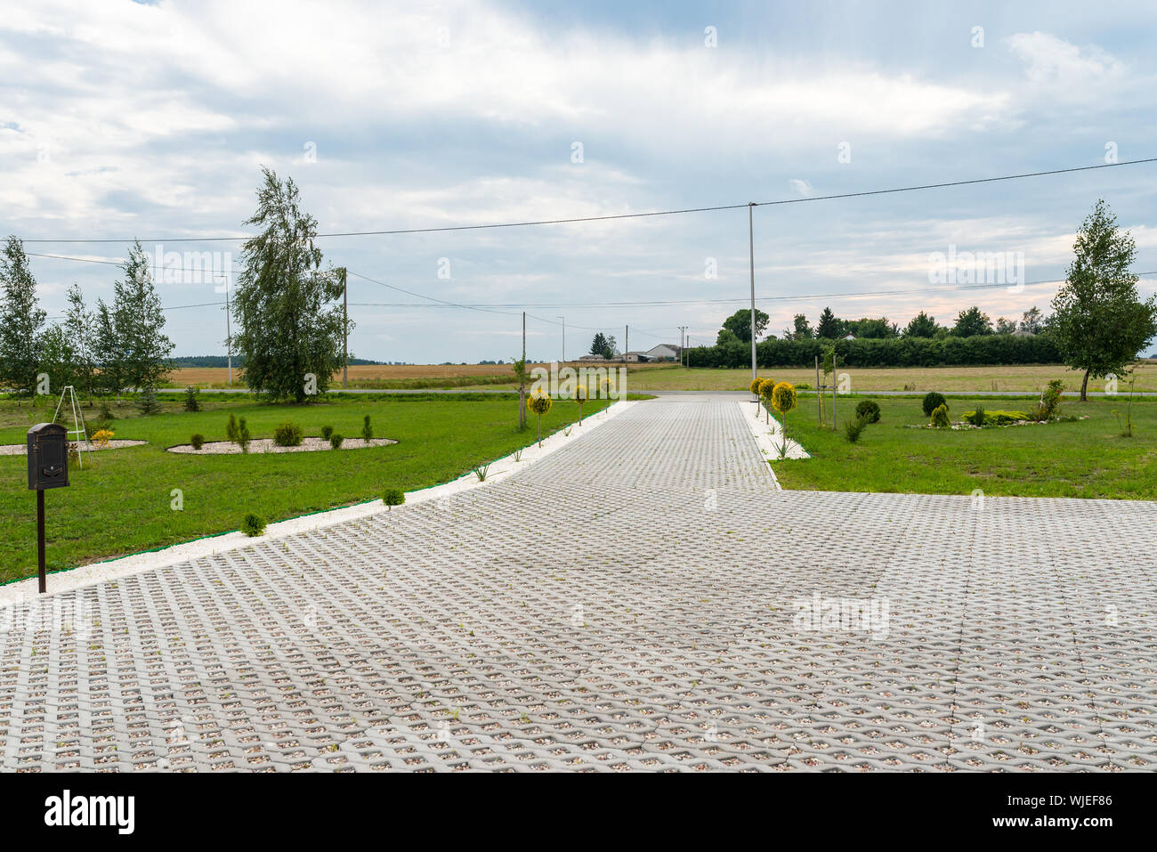 Eintrag für Autos, die in der Eigenschaft von Openwork Betondecke mit bunten Steinchen gefüllt, rund grün Gras und kleine Bäume. Stockfoto