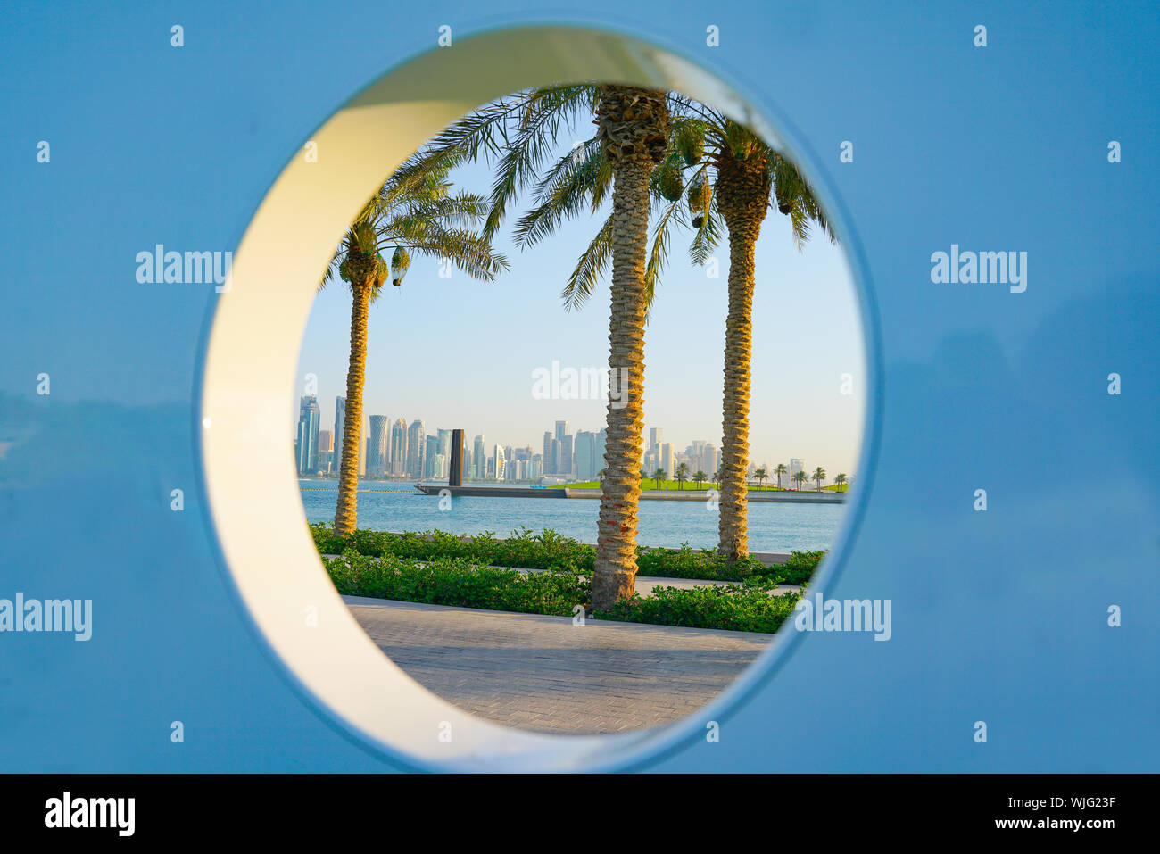 Entlang der Corniche mit Blick auf Doha's high-rise business district durch kreisförmige Bohrung mit drei Palmen und den Hafen. Stockfoto