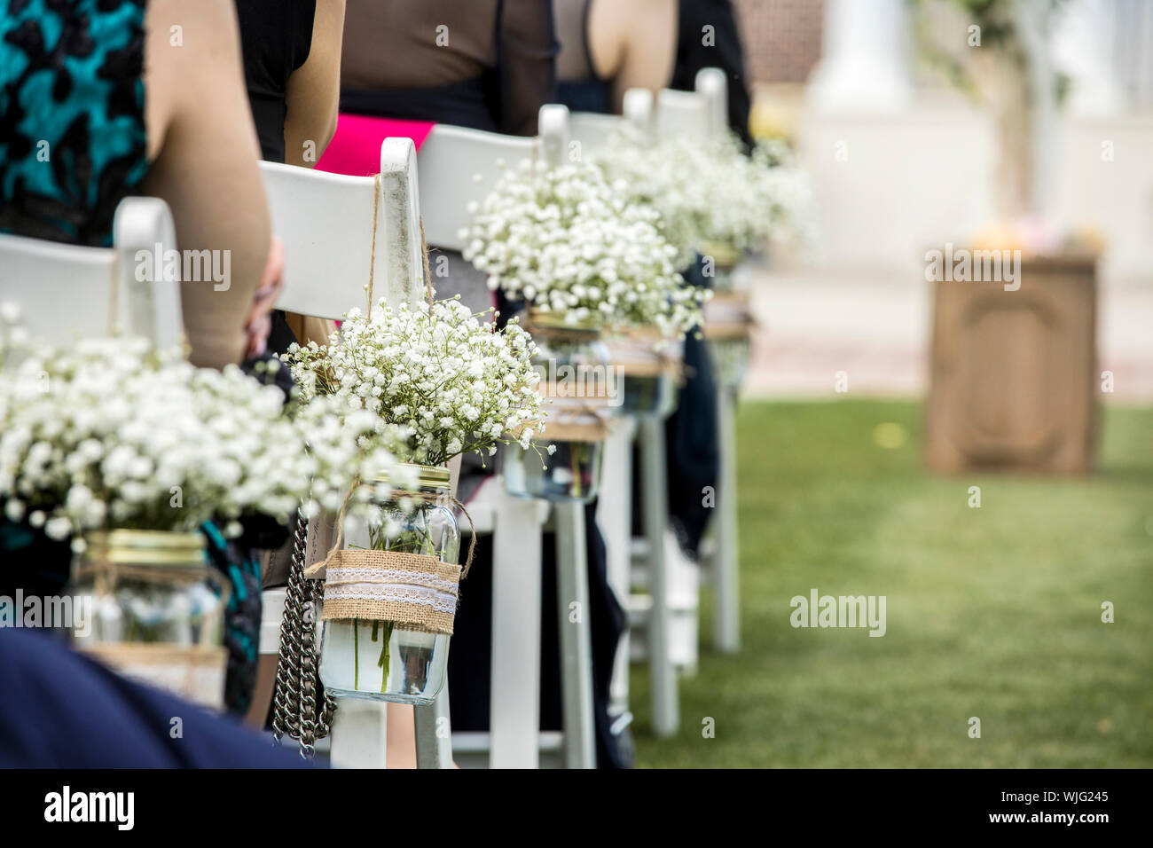 Stühle, hängende Gläser mit Blumen, und die Gäste bei der Hochzeit. Stockfoto