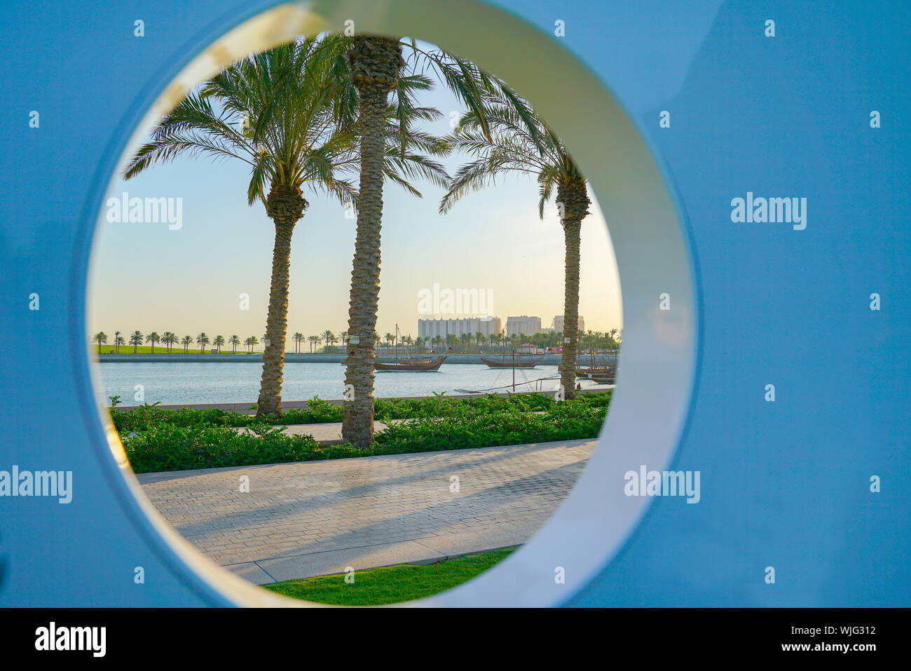 Entlang der Corniche mit Blick auf Doha's high-rise business district durch kreisförmige Bohrung mit drei Palmen und den Hafen. Stockfoto