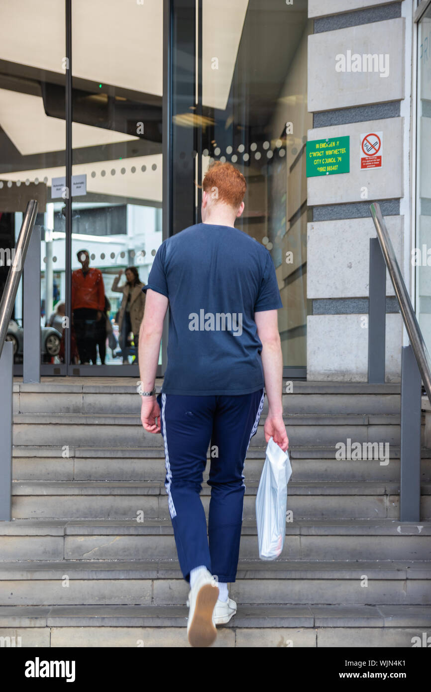 Ein Teenager zu Fuß die Treppe hinauf zu einem Einkaufszentrum mit einem Kunststoff Tragetasche Stockfoto
