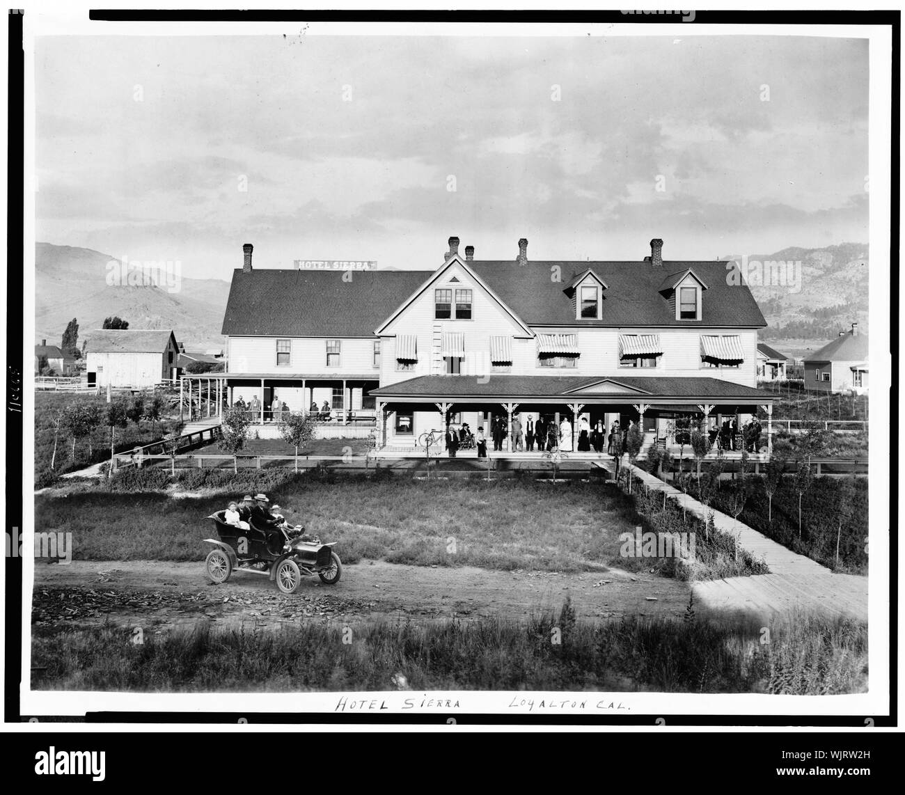 Hotel Sierra, Loyalton, Kalifornien, mit Menschen, die auf der Veranda, die Menschen im Auto im Vordergrund, und Berge im Hintergrund Stockfoto
