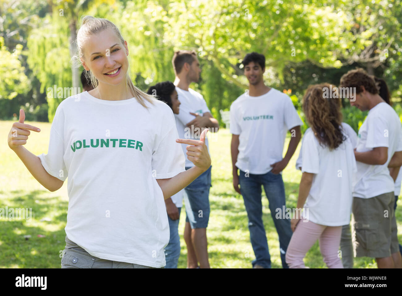 Schönen weiblichen Freiwilligen pointing at t-shirt mit Freunden im Hintergrund Stockfoto