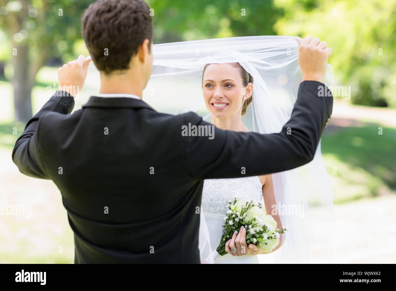 Die jungen Liebenden Bräutigam anheben Schleier der Braut in Park Stockfoto