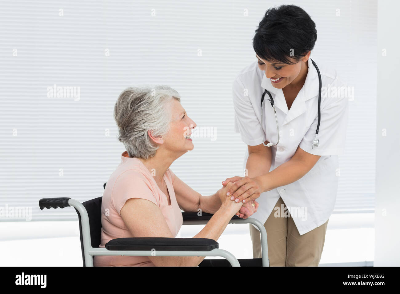 Ärztin sprechen zu einem älteren Patienten im Rollstuhl im Krankenhaus Stockfoto