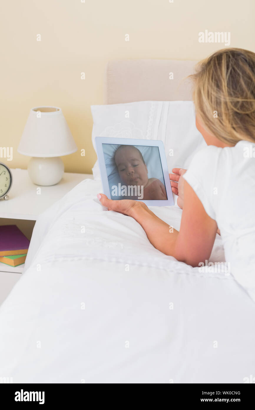Aufmerksame Frau, die mit einem Tablet-pc auf ihrem Bett liegend Stockfoto