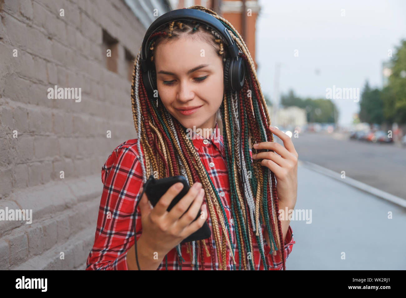 Junge Frau mit farbige Pigtails Hören von Musik über Kopfhörer auf der Straße Stockfoto