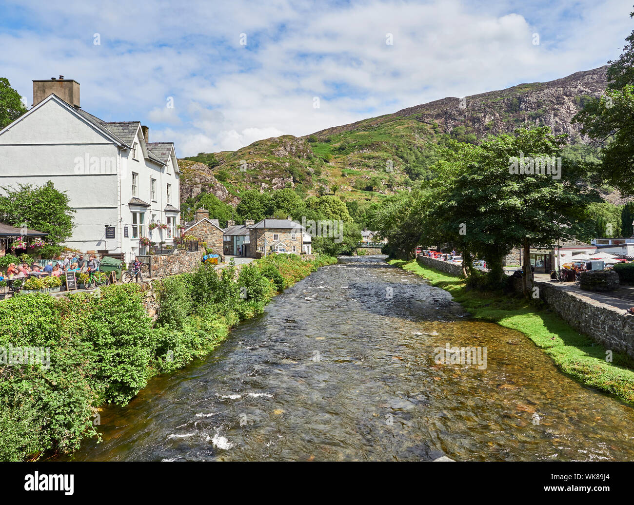 Blick auf den Fluss Glaslyn läuft durch das Dorf Beddgelert mit einem Haus und einer Straße entweder Seite an einem Sommertag Snowdonia, Gwynedd, Wales, Großbritannien Stockfoto