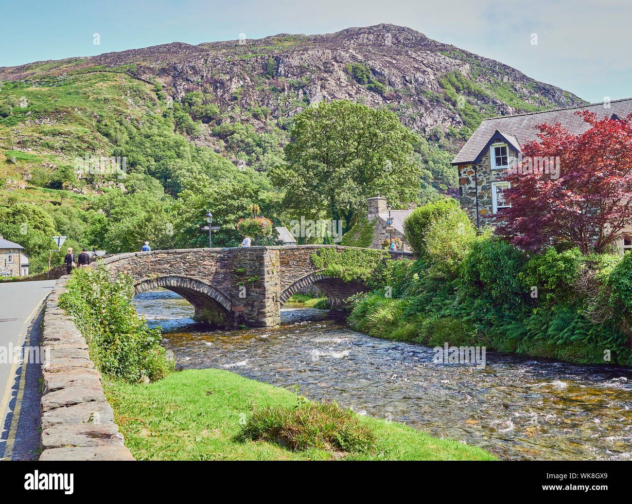 Blick auf eine Brücke aus Stein über den Fluss Glaslyn fließt durch die Stadt Beddgelert an einem Sommertag, Snowdonia, Gwynedd, Wales, Großbritannien Stockfoto