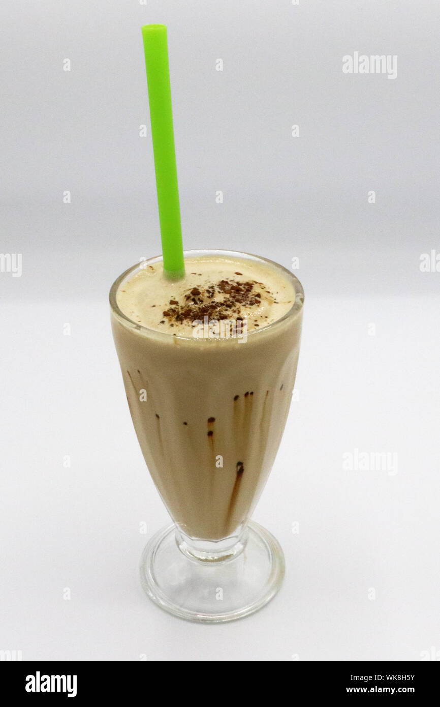 Milchshake mit Eiskaffee, serviert in einem hohen Glas mit grünem Strohhalm, gekrönt mit Kakaopulver und Schokoladenstreuer. Stockfoto