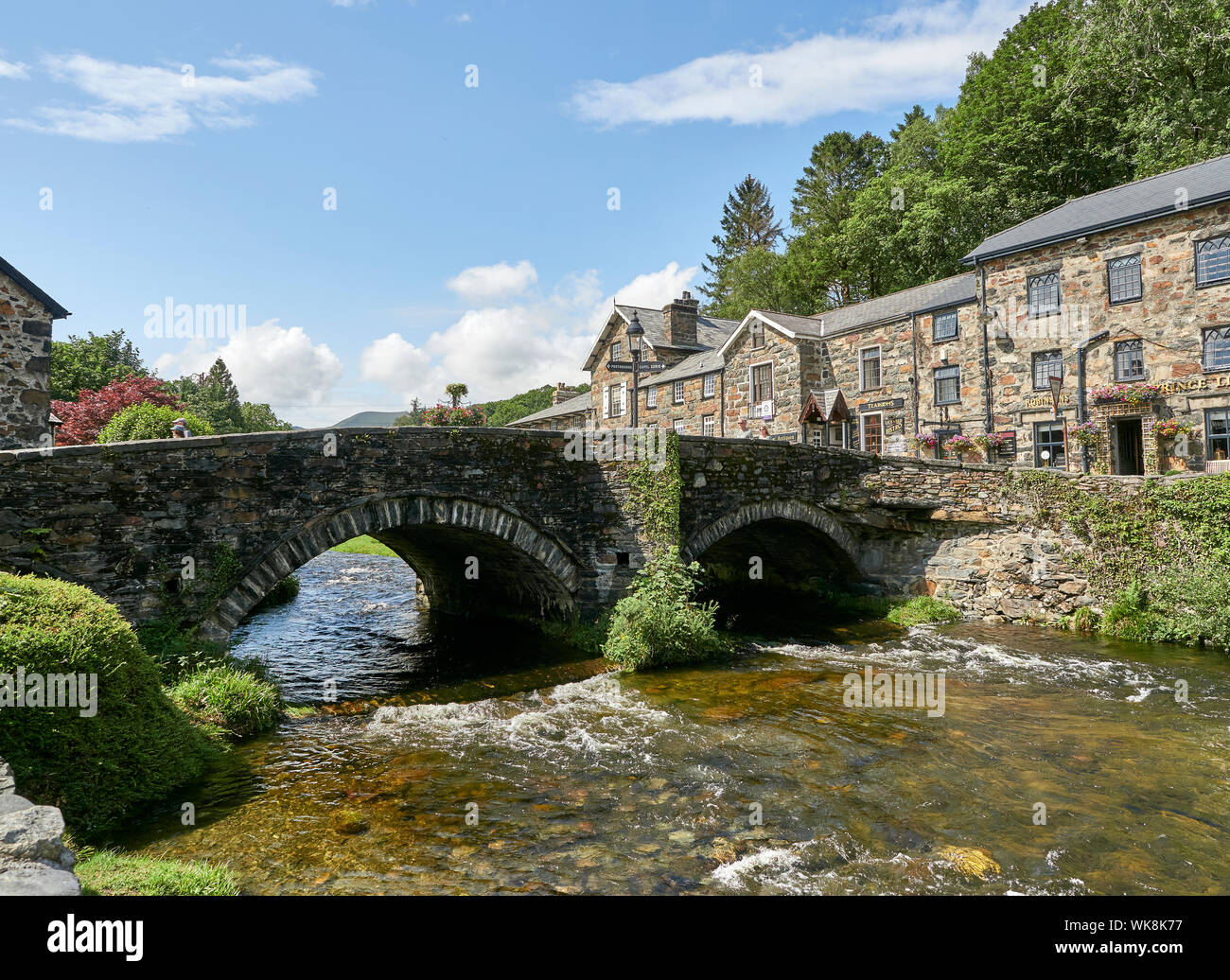 Blick auf eine Brücke aus Stein über den Fluss Glaslyn fließt durch die Stadt Beddgelert an einem Sommertag, Snowdonia, Gwynedd, Wales, Großbritannien Stockfoto