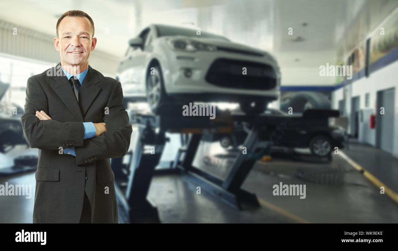 Autoverkäufer steht mit verschränkten Armen neben einem Wagen auf eine Hebebühne in der Händlerniederlassung Stockfoto