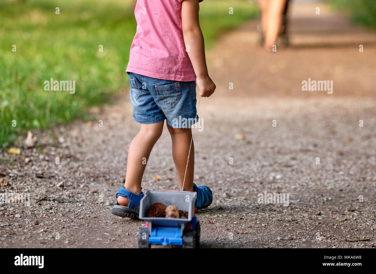 Rückansicht des unteren Abschnitt von einem 3-4 jährigen Kind im Sommer closthing Ziehen einer Spielzeug-LKW mit Kegel in Es Stockfoto