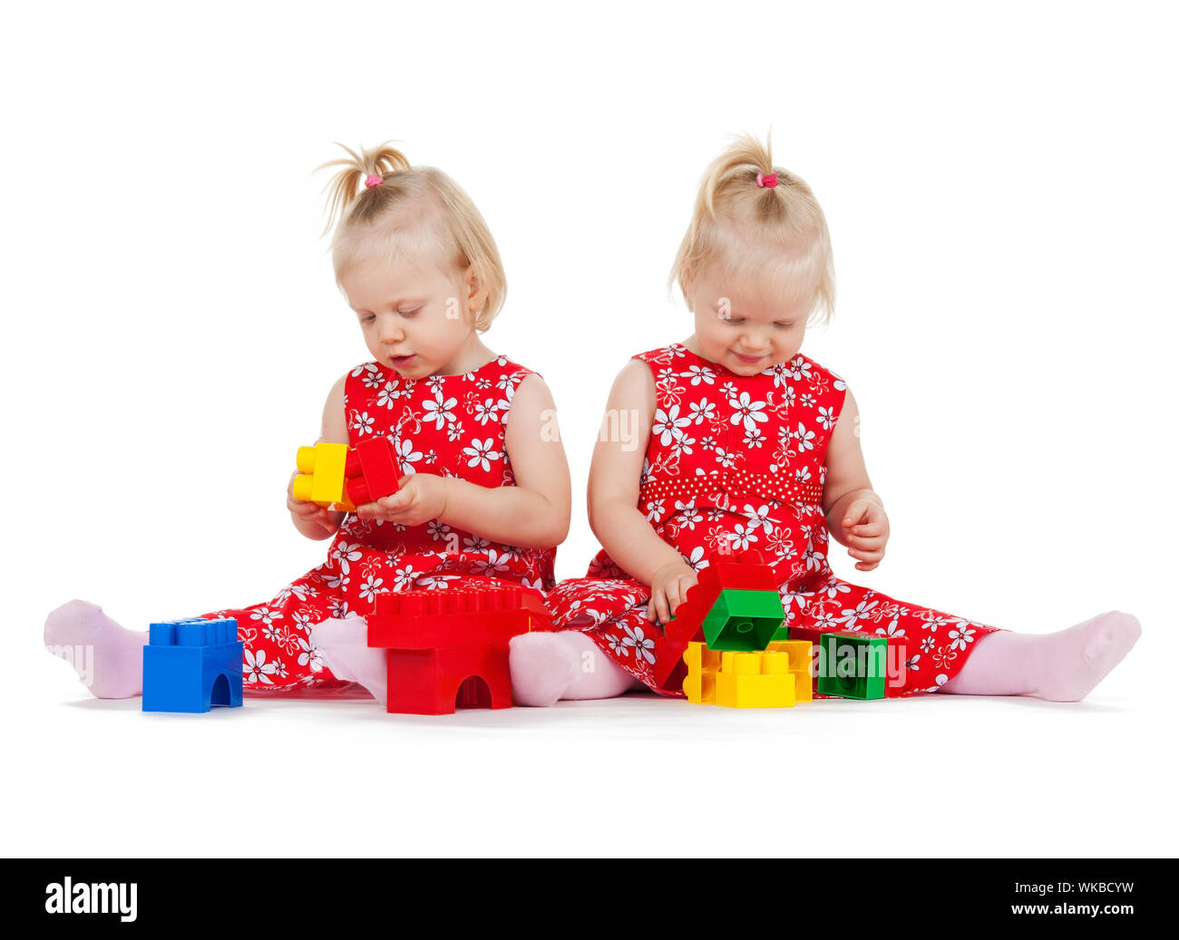 Kinder und Zwillinge Konzept - zwei eineiige Zwillinge in rot Kleider mit Klötzchen spielen Stockfoto