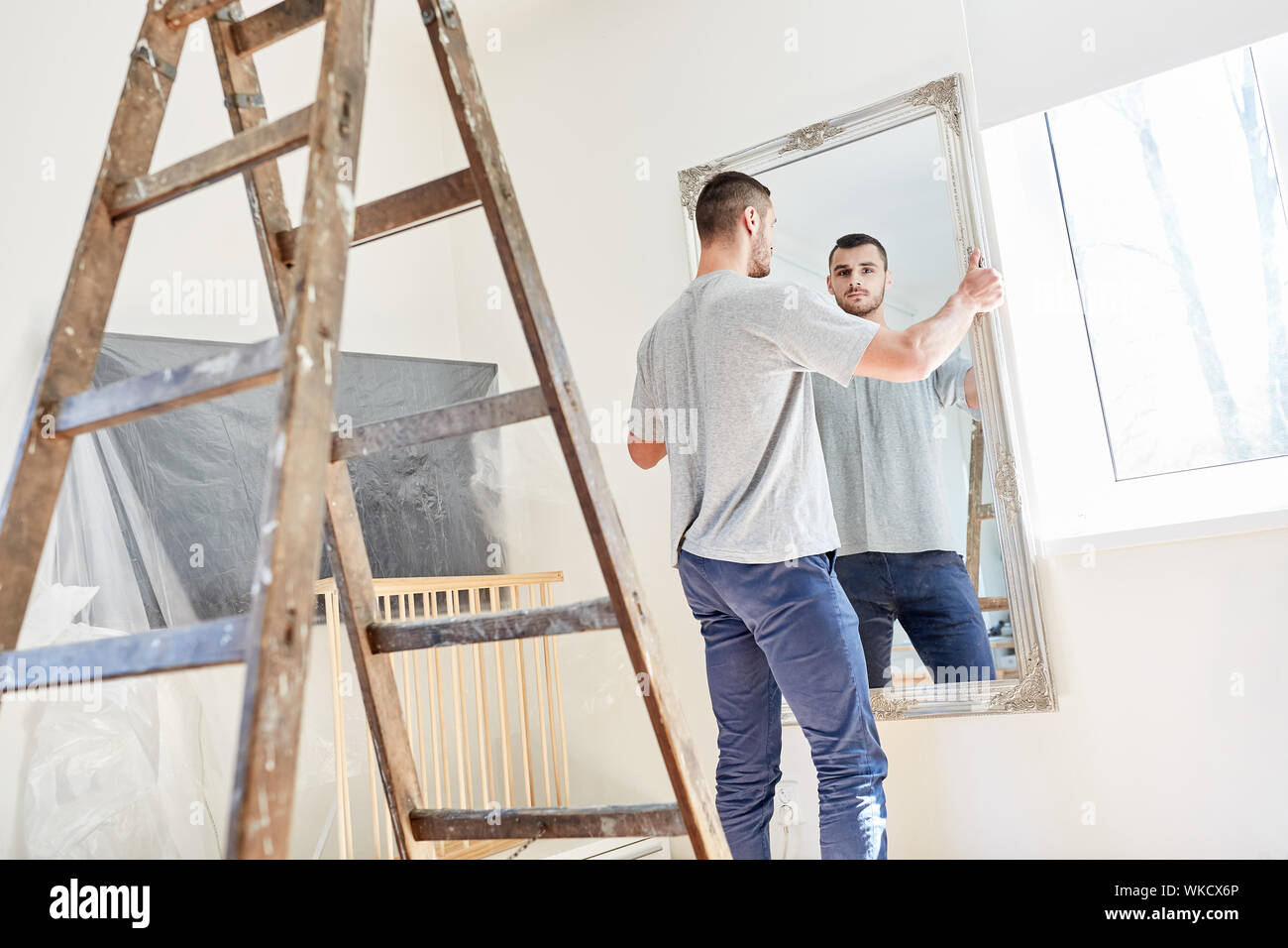 Mann aufhängen Spiegel in der neuen Wohnung während der Renovierung oder Umzug Stockfoto