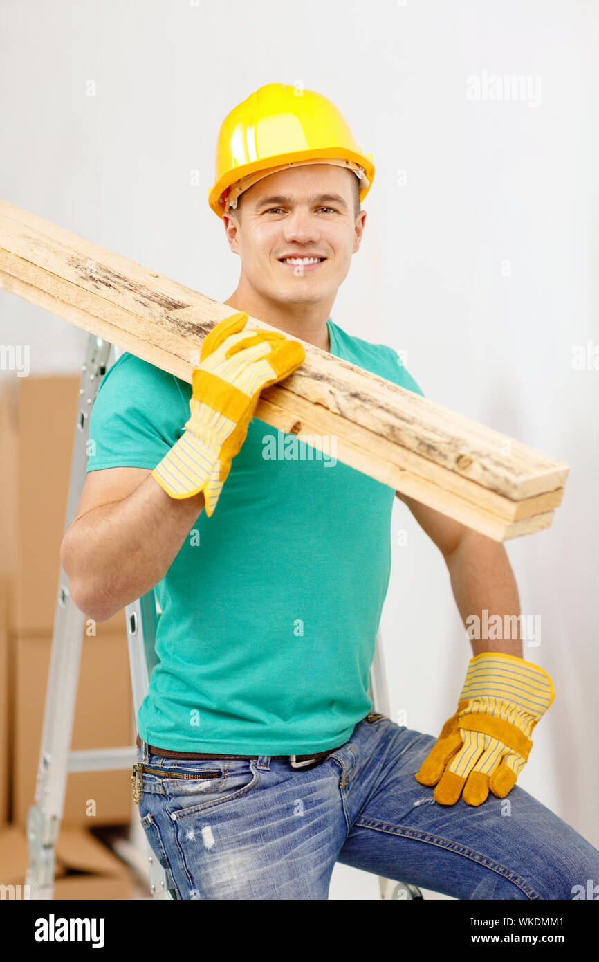 Reparatur, Bau und Instandhaltung Konzept - lächelnd männliche Arbeiter in Schutzhelm tragen Holzbretter Stockfoto