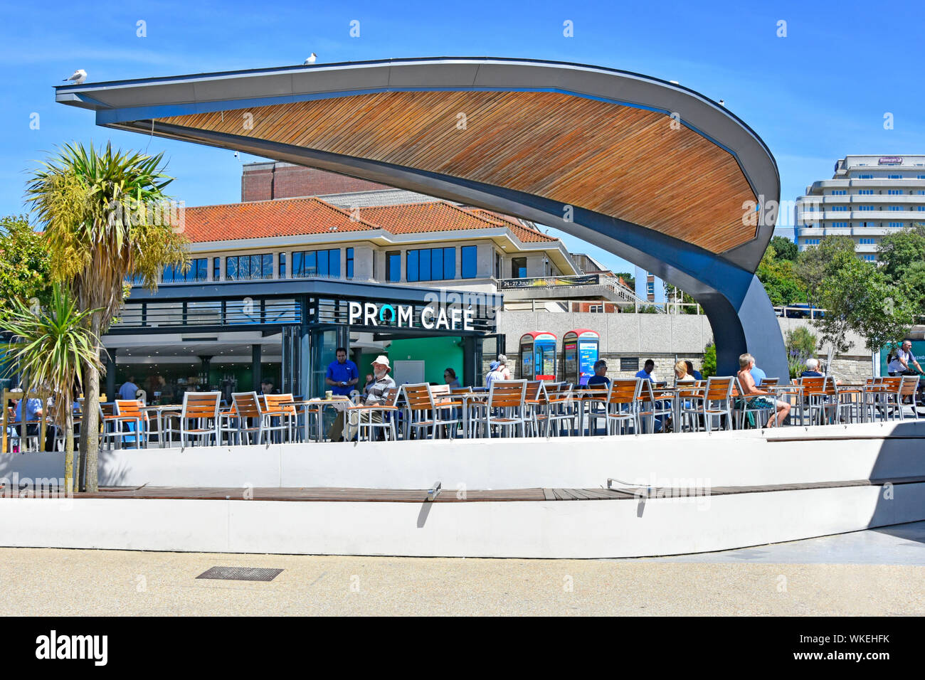 Die Gäste, die im Sommer auswärts essen, bieten Schatten und Schutz in der Nähe des Prom Cafe Shops im Bournemouth Beach Resort Dorset England UK Stockfoto