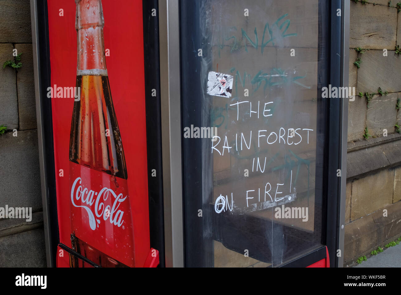 "Der Regenwald Brennt" Graffiti auf der Seite der British Telecom Telefon Box mit einem Coca-Cola-Werbung, Liverpool, Großbritannien. Stockfoto