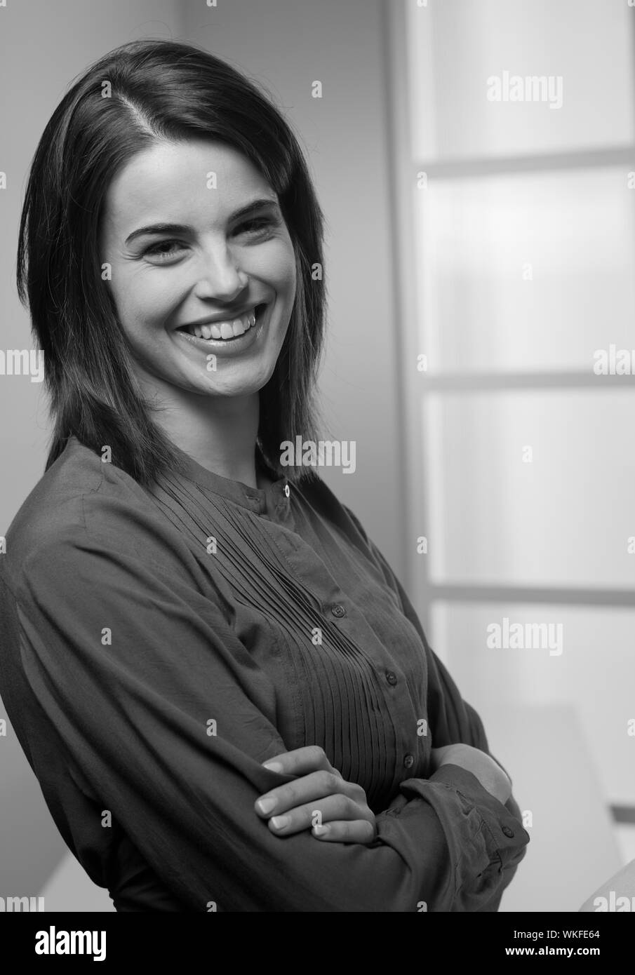 Attraktive junge Frau lächelnd mit verschränkten Armen. Stockfoto