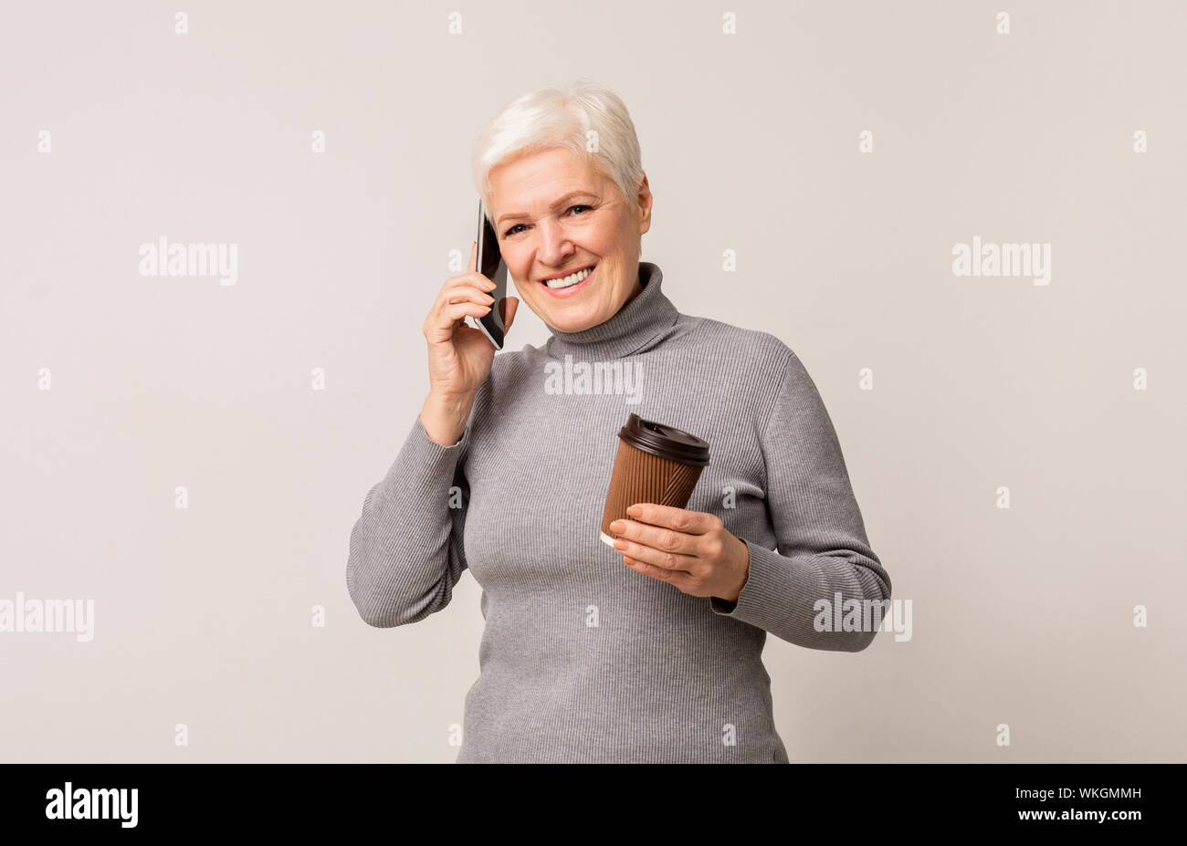 Ältere Frau mit Tasse Kaffee und Reden auf dem Smartphone Stockfoto