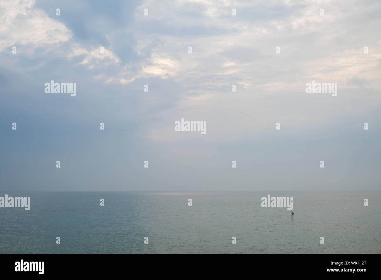 Eine friedliche bewölkter Himmel über ein ruhiges Meer mit einem einzigen groyne Marker. Stockfoto