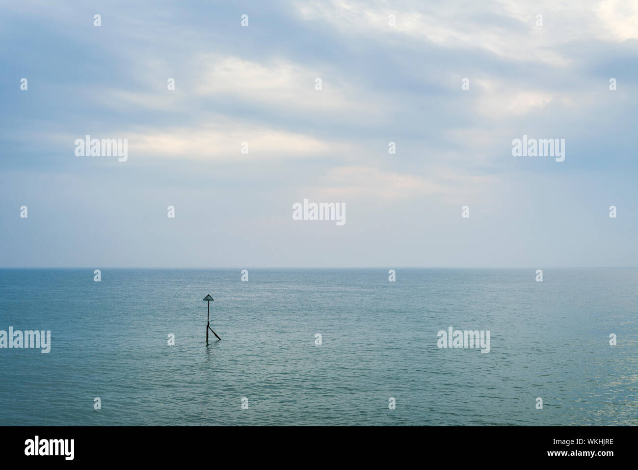 Eine friedliche bewölkter Himmel über ein ruhiges Meer mit einem einzigen groyne Marker. Stockfoto