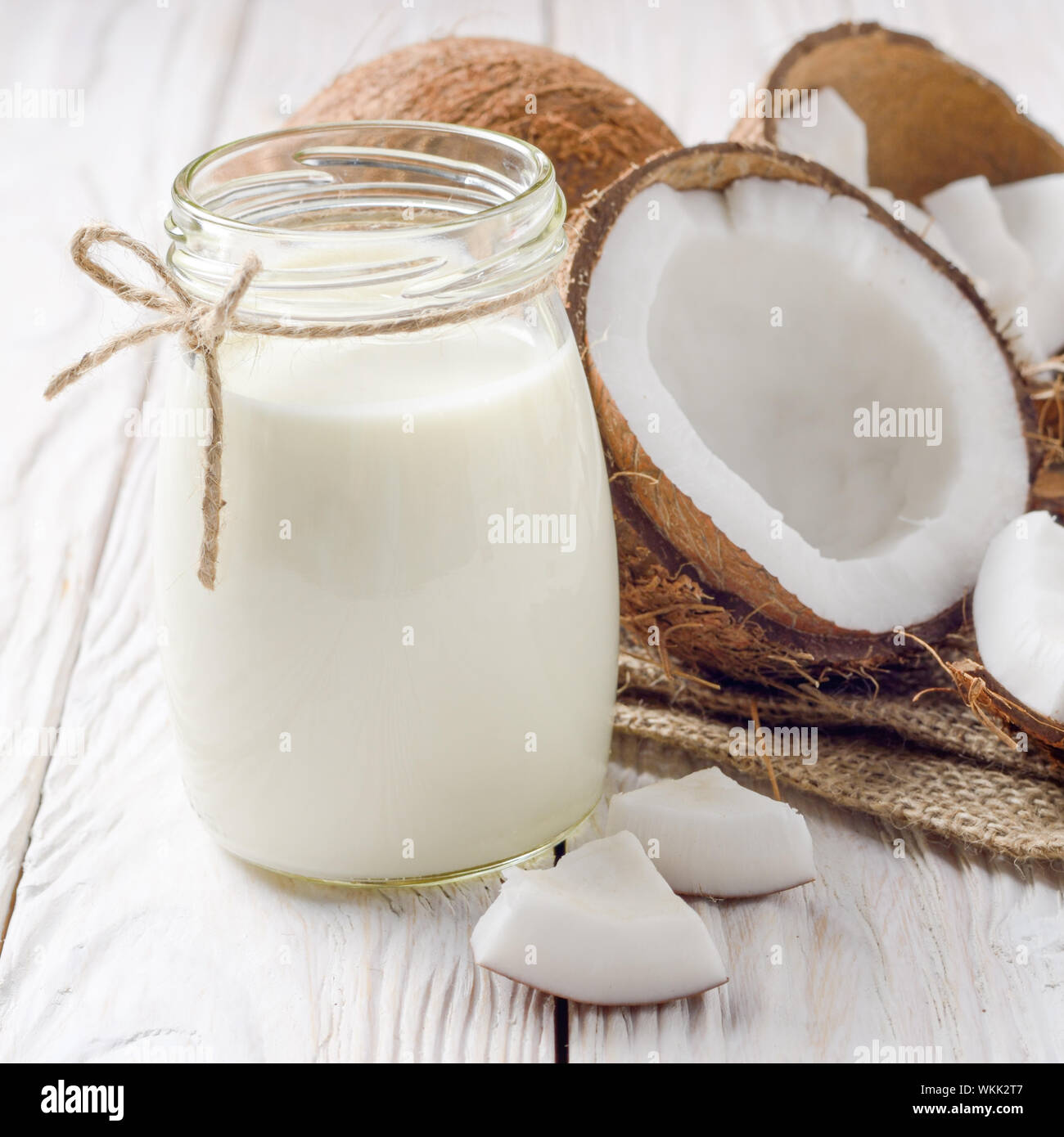 Mason jar von Milch oder Joghurt auf Hanf Serviette auf weiße Holztisch mit Kokosnuss beiseite Stockfoto