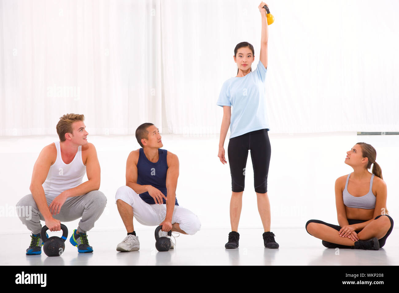 Gruppe von unterschiedlichen Menschen auf der Suche Frau heben Kettlebell in Turnhalle Stockfoto