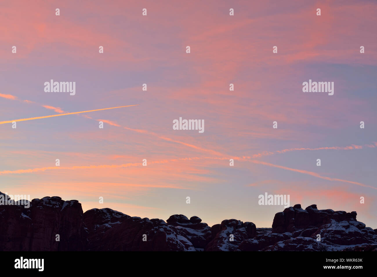 Sonnenuntergang Himmel mit Flugzeug Kondensstreifen über eine verschneite Landschaft, Arches National Park, Utah, USA Stockfoto