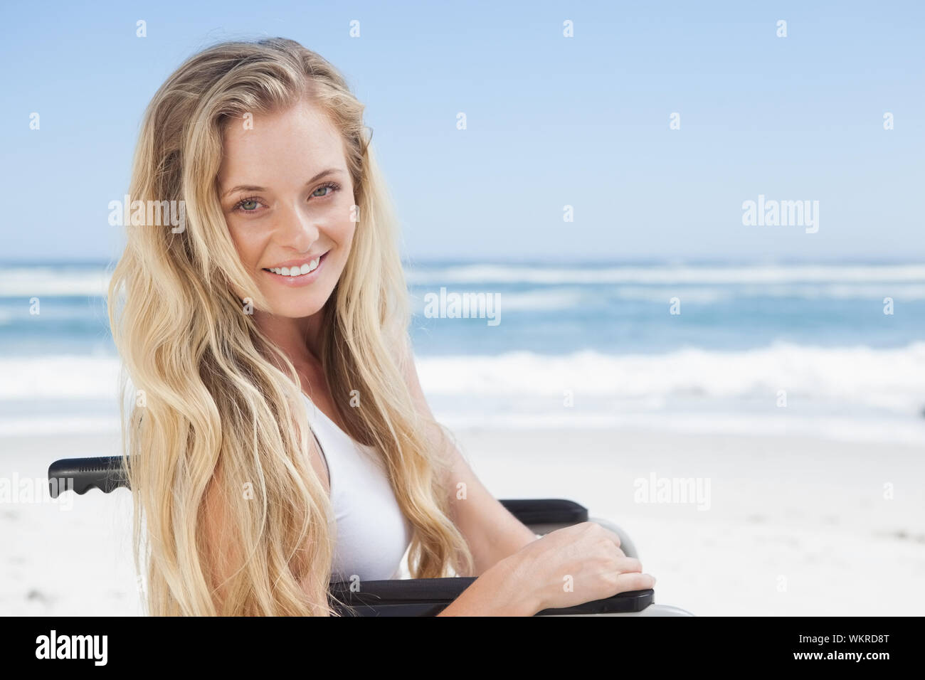 Rollstuhl blond lächelnd in die Kamera am Strand an einem sonnigen Tag gebunden Stockfoto