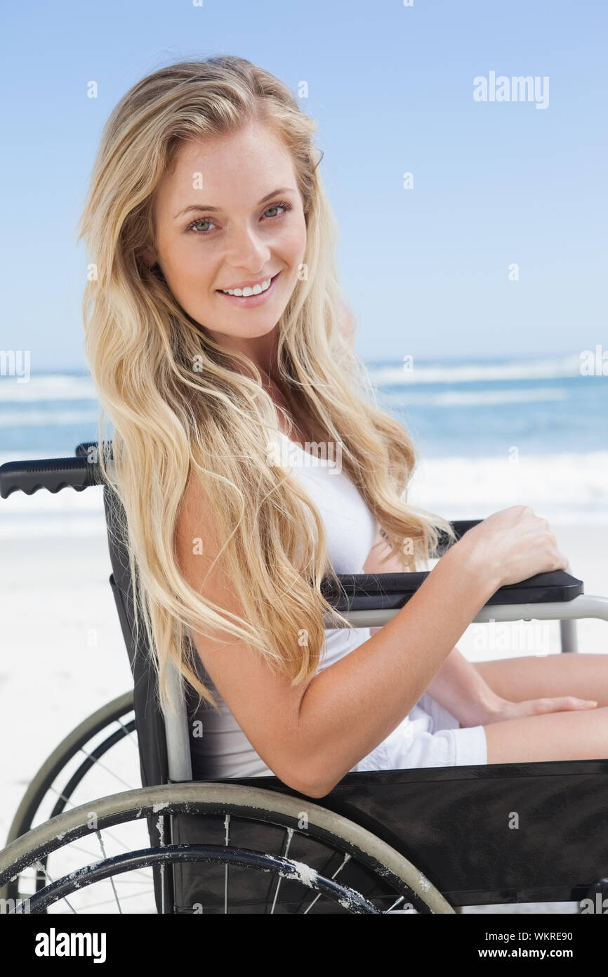 Rollstuhl blond lächelnd in die Kamera am Strand an einem sonnigen Tag gebunden Stockfoto