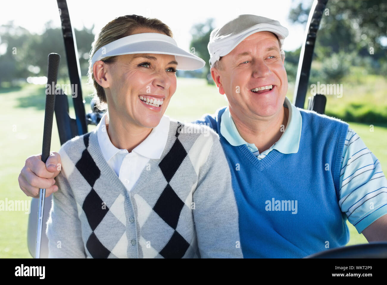 Viel Spaß paar im Golf Buggy lächelnd an einem sonnigen Tag auf dem Golfplatz sitzen Stockfoto