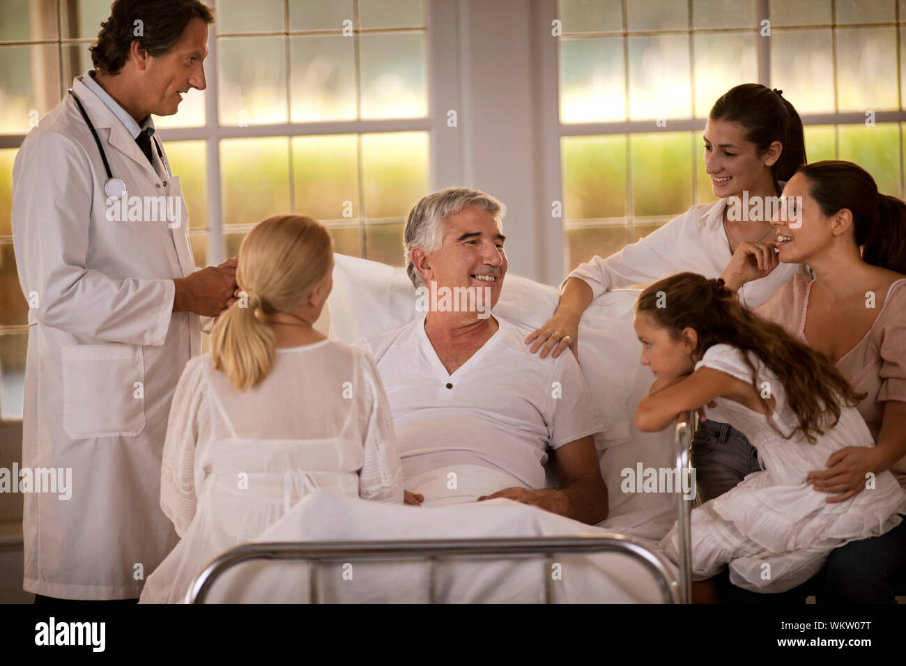 Familie von Frauen besuchen Sie einen männlichen Verwandten im Krankenhaus, während ein Arzt an seinem Bett steht. Stockfoto