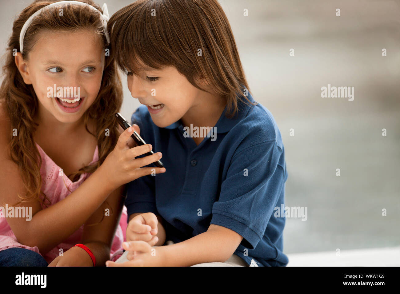 Ein Junge und ein Mädchen lächeln verschmitzt, als sie schauen auf ein Handy. Stockfoto